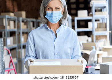 Older business woman retail seller, entrepreneur, small business owner wears face mask and gloves for covid 19 protection looking at camera holding parcel box standing in delivery warehouse, portrait. - Powered by Shutterstock