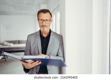older businessman with glasses holds a folder and looks into the camera