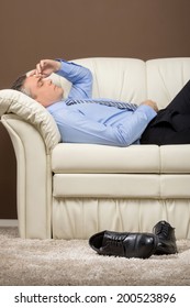 Older Businessman Lying On White Sofa. Man Took Off Shoes And Sleeping On Couch