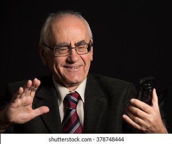 Older Businessman, Wearing Eyeglasses On Black Background, Uses Smart Phone, Has Video Chat