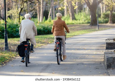 Older Caucasian Couple Riding Bicycles Through Public Park Together. Back View