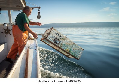 older, caucasian Man in overalls standing on boat throwing lobster trap into water, Maine, USA