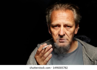 Older Caucasian Man Smoking Cigarette On Dark Background