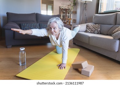 Older caucasian woman in sportswear doing gymnastic exercises on the living room floor with a mat - Powered by Shutterstock