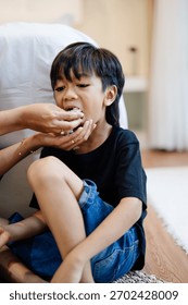 An older child eats while a parent feeds him, creating a natural and intimate family moment in an indoor home setting.