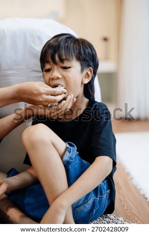 An older child eats while a parent feeds him, creating a natural and intimate family moment in an indoor home setting.