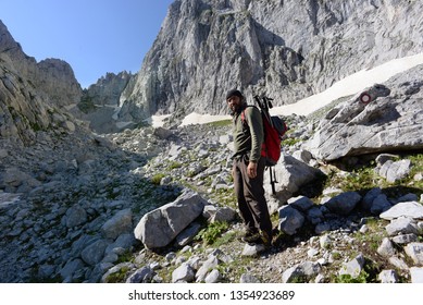 Older Chubby Hiker On His Way Up A Mountain With Cliffs Around Him