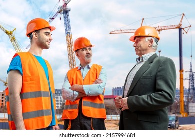 Older Construction Supervisor With Younger Worker Helper At Construction Site. Managers Wearing Protective Workwear, Hard Hat, Construction Cranes On Skyline. Construction Workforce, Working Labor Man