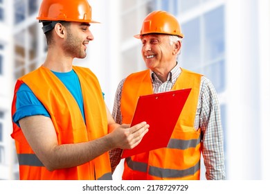 Older Construction Supervisor With Younger Worker Helper At Construction Site. Managers Wearing Protective Workwear, Hard Hat, Construction Scaffolding. Construction Workforce, Working Labor Man.