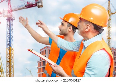 Older Construction Supervisor, Younger Worker Helper At Construction Site. Managers Wearing Protective Workwear, Hard Hat, Construction Cranes On Skyline. Construction Workforce, Working Labor Man.