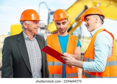 Older Construction Supervisor With Younger Worker Helper At Construction Site. Managers Wearing Protective Workwear, Hard Hat, Bulldozer, Excavator. Construction Workforce, Working Labor Man.