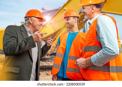 Older Construction Supervisor With Younger Worker Helper At Construction Site. Managers Wearing Protective Workwear, Hard Hat, Bulldozer, Excavator. Construction Workforce, Working Labor Man.