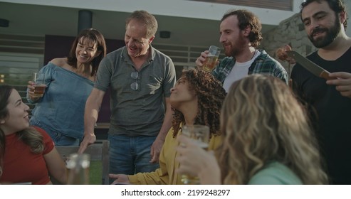 Older Couple Arriving At Backyard Barbecue Garden Party. Group Of Friends Welcoming Parents Celebrating Life With Food And Leisure. Happy People Toasting With Glasses