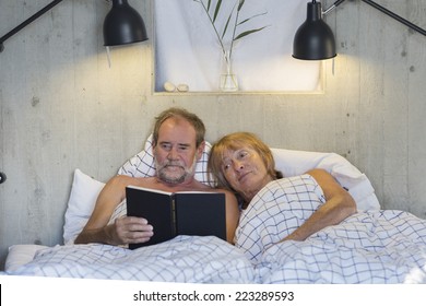 Older Couple In Bed Reading A Book