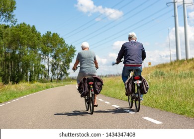 Older Couple Biking On Asphalt Road In The Dutch Village Of Leiderdorp. Bike With Hearing Impaired Sign.