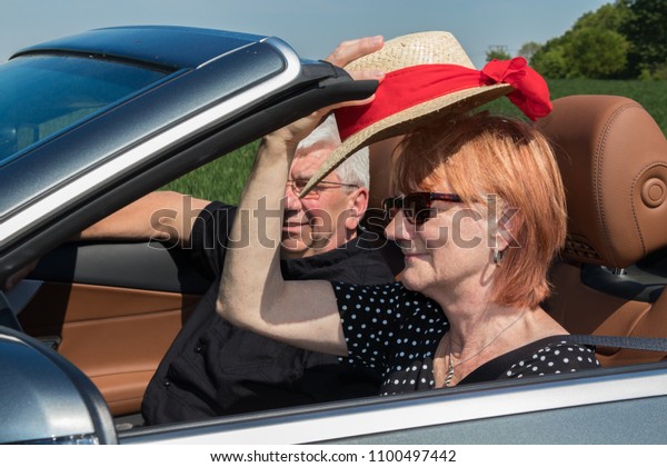 older couple drives with a luxury convertible car on\
a sunny day
