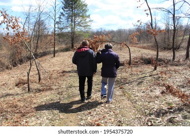 Older Couple Faced Backwards, Walking Through The Forest. These Days It's Important To Spend Time Outside And In Nature, Especially For Older People. Walking Is Always A Good Choice For Health.