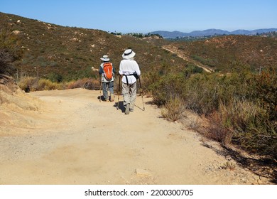 An Older Couple Hiking With Waking Poles, Backpack And Sun Hats.