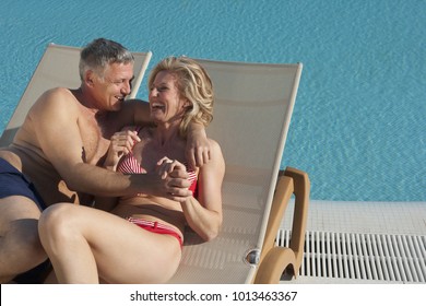 Older Couple Laughing On Sunbeds By Pool