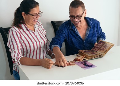 Older Couple With A Photo Album In The Living Room Of Their Home