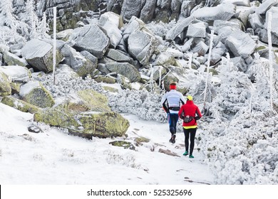 Older Couple Running Together On Winter Mountain Trail Covered With Snow In Freezing Temperatures