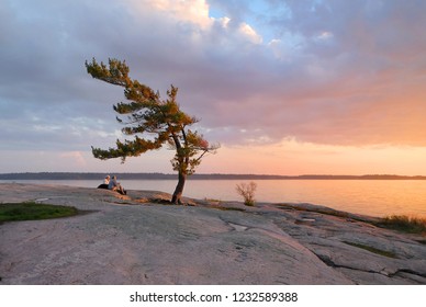 Older couple seniors watching sunset from rocky shore over the lake, orange pink clouds and soft light. Sunset at Killbear Provincial Park, Ontario, Canada. Relaxation, tranquility, camping concept. - Powered by Shutterstock