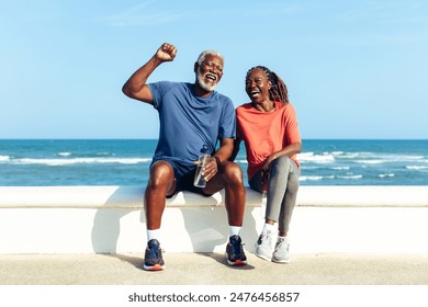 An older couple shares a light-hearted moment by the sea, laughing together while sitting on a low wall, showcasing lifelong health, companionship and happiness. - Powered by Shutterstock