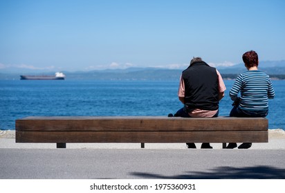 Older Couple Sitting On The Beach Looking In The Distance At The Sea