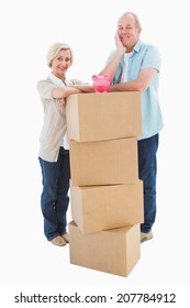 Older Couple Smiling At Camera With Moving Boxes And Piggy Bank On White Background