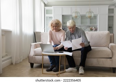 Older Couple Sorting Out Utility Bills, Making Monthly Payments, Using E-bank On Laptop Looking Serious Or Concerned Due To High Electricity Rates, Mistake In Papers Sitting On Sofa At Home. Finances