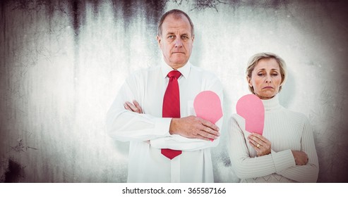 Older Couple Standing Holding Broken Pink Heart Against Grey Background