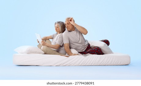 Older couple using tablet and reading newspaper on bed in clean studio scene. Concept of digital media, print versus online reading, telecom ads and home lifestyle promotion.