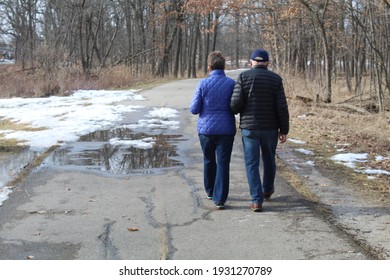 Older Couple Walking Arm And Arm At Miami Woods In Morton Grove, Illinois During A Spring Thaw On The North Branch Trail