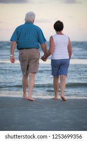 Older Couple Walking On The Beach At Sunset