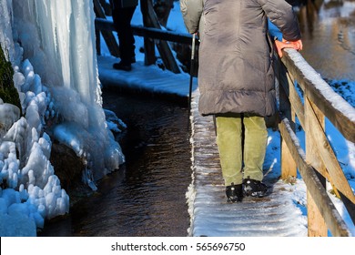 Older Couple Walking Over A Planked Footbridge At A Frozen Waterfall