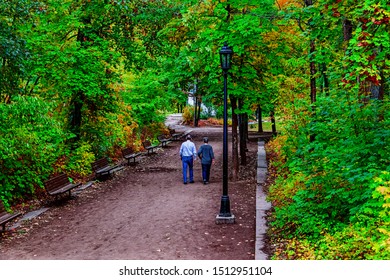 Older Couple Walking In The Park With Vintage Street Lights And Benches