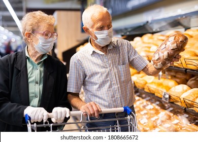 Older European Couple Wearing Mask And Gloves With Covid Protection Chooses Buns And Bread In Supermarket Bakery