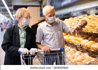 Older European Couple Wearing Mask And Gloves With Covid Protection Chooses Buns And Bread In Supermarket Bakery