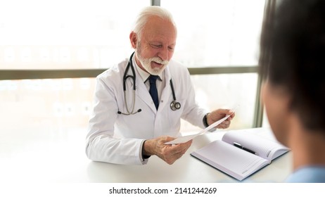 Older Experienced Doctor Reviewing Patient Electrocardiogram During Consultation In The Hospital. Satisfied Doctor Looking Latest Lab Results Of His Patient After Long Treatment