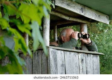 Older, experienced hunter sitting on his hunting pulpit and looking through his binoculars. - Powered by Shutterstock