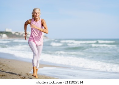 Ältere Frauen, die Sport treiben, um fit zu bleiben. Reife Frau, die am Strand entlang läuft. Konzept des gesunden Lebens im Alter. Senior Women in Fitnesskleidung am Strand