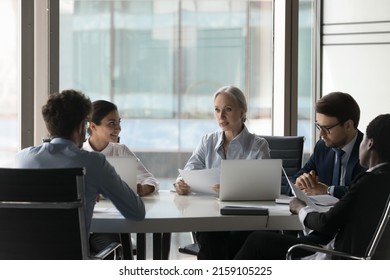 Older female executive manager teach diverse staff, take part in group meeting in office boardroom, analyze, make paperwork review, develop marketing plan, explain new strategy to workers at briefing - Shutterstock ID 2159105225