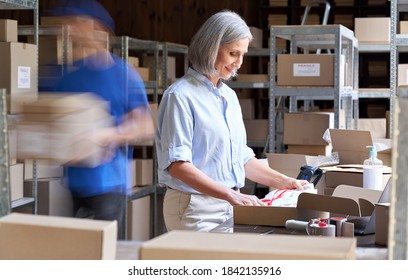 Older Female Small Business Owner Worker Packing Post Shipping Ecommerce Retail Order In Box In Warehouse With Courier Hurry In Blur Motion To Deliver Parcels. Fast Speed Express Rush Delivery Concept