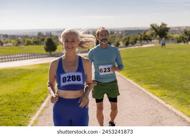 older friends run marathon in the park. Senior mature couple running together in competition in the park while the woman wins in the front line - Powered by Shutterstock