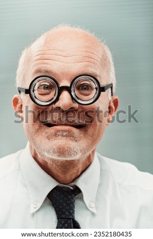 Older gentleman, silly look, ultra-thick spectacles, humorously personifies a socially challenging yet deserving character. Formal setting, white shirt, tie