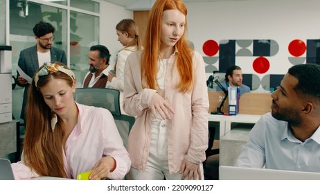 An Older Handsome Business Man Talking With His Two Work Colleagues And Advising Them While A Woman With Ginger Hair Is Talking To Her Assistants About The Work Their Doing, In A Modern Looking Office