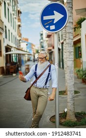 Older Hipster Man Using A Smartphone And Playing Music, Having Fun With Mobile Phone Technology While Holding On To A Traffic Sign In The City - Happy, Technological And Cheerful Senior Lifestyle 