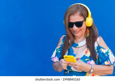 Older Hispanic Woman Listening To Music On The Phone In The Street.