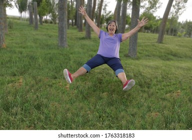 
Older Lady, Older Woman, Grandmother, Jumping For Joy On The Lawn. Positivism And Energy