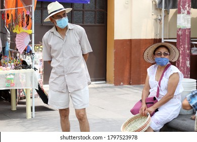 
Older Latino Couple With Protective Face Masks And Hat Walking In The Plaza, New Normal Covid-19